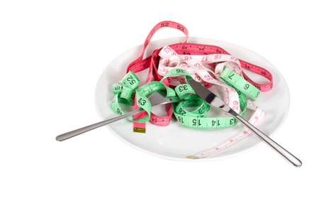 Knife and fork with tape measures on a plate as though served as food in a weight loss, wellness and dieting concept isolated on whiteの写真素材