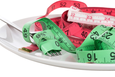 Dieting or weight loss concept with a fork entwined in colorful tape measure on a generic white plate as though served as food in a close up partial viewの写真素材