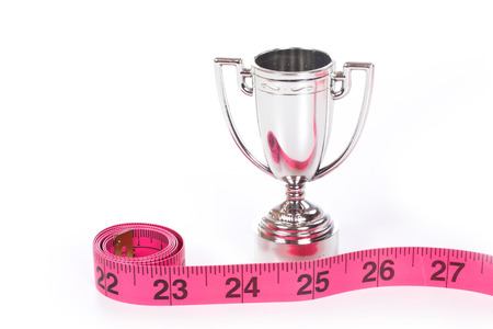 Red measuring tape roll marked in inches and small silver sports cup close-up isolated on white background with copy spaceの写真素材