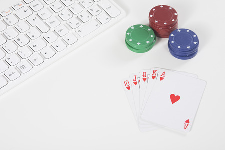 White plastic keyboard next to red green and blue colored poker chips and red and white playing cardsの写真素材