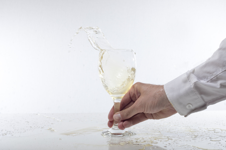 Man splashing white wine in a glass in a motion freeze image of the splash over a white background with copy spaceの写真素材