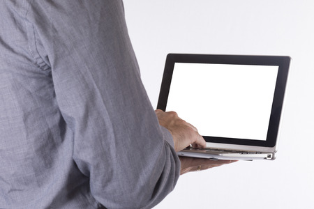 Man holding a laptop with blank white screen typing with his fingers in a close up over the shoulder viewの写真素材