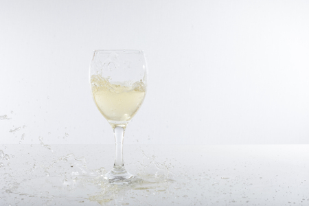 Fresh, crisp champagne splashes into a wine glass and spills on to a white bar bench top with copy space.の写真素材