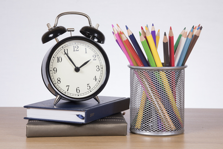 Stacked books with an alarm clock and coloured pencils on a timber desk in a time to learn, back to school theme.の写真素材