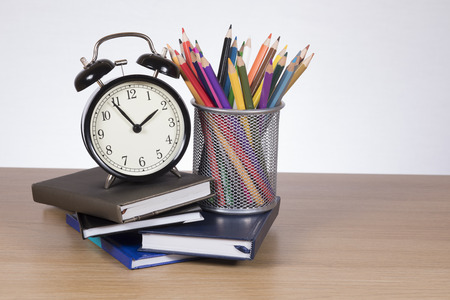 An arrangement of school learning supplies including books, coloured pencils and an alarm clock on a wooden desk.の写真素材