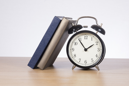 Two books leaning against alarm clock standing on wooden deskの写真素材