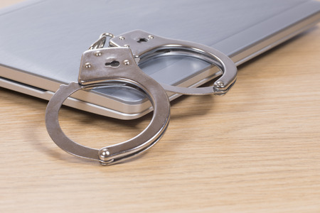 Handcuffs on a closed laptop computer conceptual of online crime , hacking and identity theftの写真素材