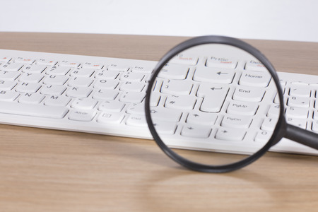 Computer keyboard enlarged through a magnifying glass in a conceptual image of analysis and online researchの写真素材