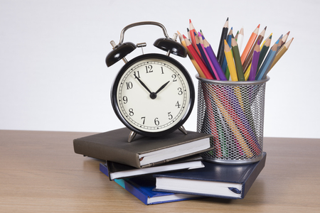 Alarm clock standing on pile of planners with colored pencils in containerの写真素材