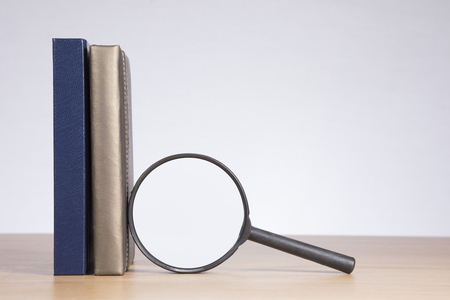 Magnifying glass with a business diary and journal standing upright on a wooden desk with large copy space on a blank white wall behindの写真素材