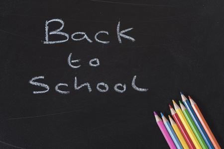 Back to School concept with a colorful set of pencil crayons in the corner of a blackboard with handwritten chalk textの写真素材
