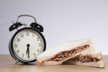 Alarm clock standing by sandwich with meat on tableの写真素材