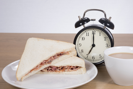 Alarm clock standing between meat sandwich served on plate with cup of coffeep of coffeeの写真素材