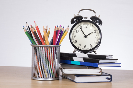 Colored pencils in container with alarm clock standing on pile of notebooksの写真素材