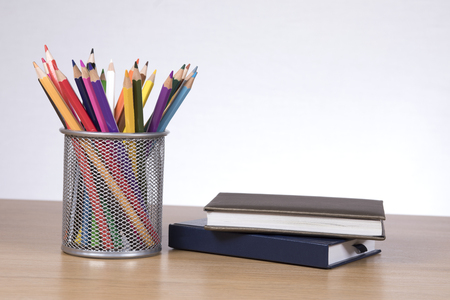 Colore pencils in container standing by two notebooks on desk against plain backgroundの写真素材