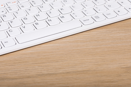 White computer keyboard on a wooden desk in a diagonal view with copy space on textured woodgrainの写真素材