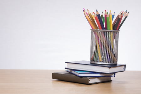 Holder with colored pencils standing on pile of books against plain backgroundの写真素材