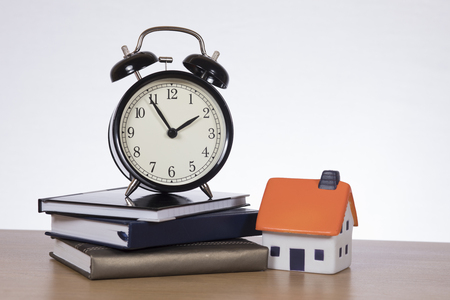 Alarm clock standing on pile of books by miniature of houseの写真素材