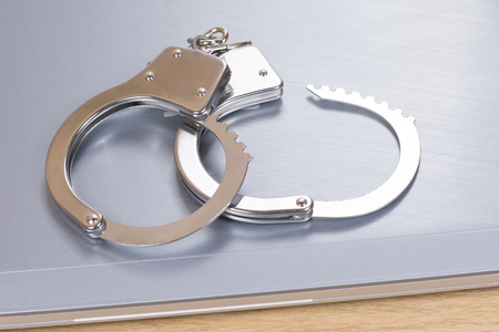 Unlocked pair of handcuffs on a closed laptop computer in a concept of online ransomware, fraud, crime, identity theft or hacking and law enforcementの写真素材