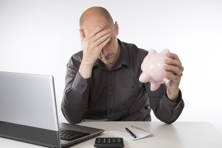 Worried man trying to balance his accounts shaking his piggy bank upside down in an effort to find more moneyの写真素材