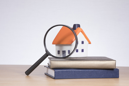 A model house on a stack of bank books under a magnifying glass with white copy space in a real estate market research themed concept.の写真素材