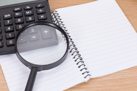 Open blank spiral binder with calculator and magnifying glass on wooden deskの写真素材