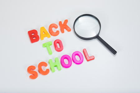 Back to school written in colourful alphabet learning letters alongside a magnifying glass with plain white background and copy space.の写真素材