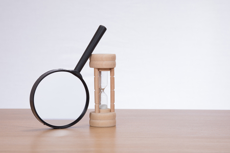 Magnifying glass leaning against sandglass on plain backgroundの写真素材