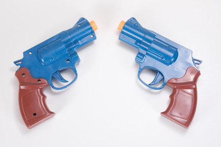 Two plastic toy handguns pointed towards each other on a plain white background with copy space.