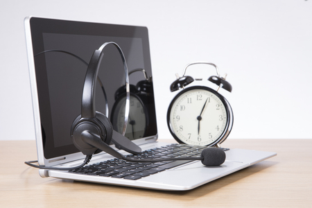 Alarm clock standing on desk by headset on laptop keyboardの写真素材