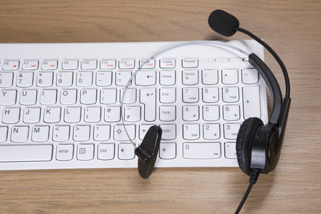 Telemarketing, call centre or client services concept with a headset with microphone on top of a white computer keyboard on a deskの写真素材