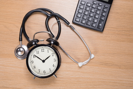 High angle view of acoustic stethoscope among alarm clock with calculator against wooden backgroundの写真素材