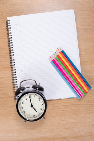 High angle view of alarm clock with colored pencils lying on blank spiral binderの写真素材