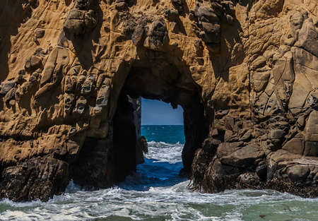 A hole in a rocky peak in the pacific ocean which looks like a door through which we can see the horizon.の写真素材