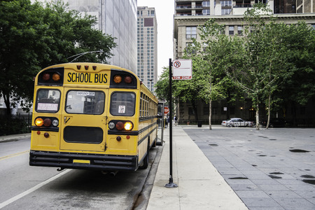 A school bus parked in a street, waiting the end of the class with the front door open, in dull weather. Back view.の写真素材