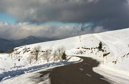 A snowy road curve in the Vosges mountains (France) in winter with a dramatic cloudy sky - december 2017の写真素材