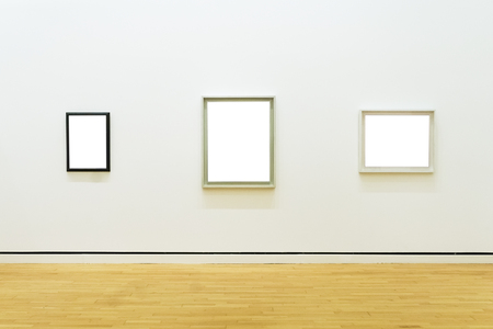 Three white clipped paintings with wooden carved frames hung on a clear wall.の写真素材