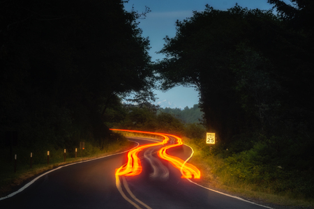 Car tail light trails on a winding road at night in forest.の写真素材