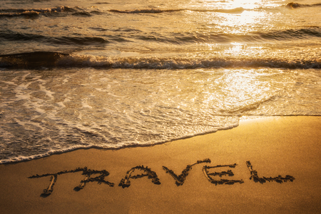 Travel text written in the sand during sunset over the ocean. Travel concept.の写真素材