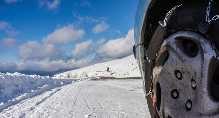 Closeup of snow chains mounted on a snowy car wheel with large copy space on its left.の写真素材