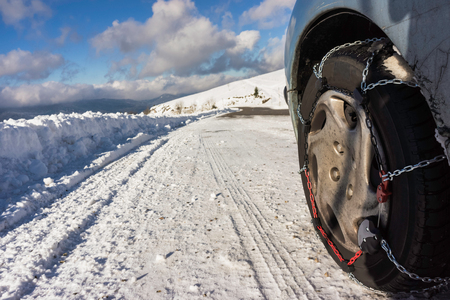 Closeup of snow chains mounted on a snowy car wheel with large copy space on its left.の写真素材