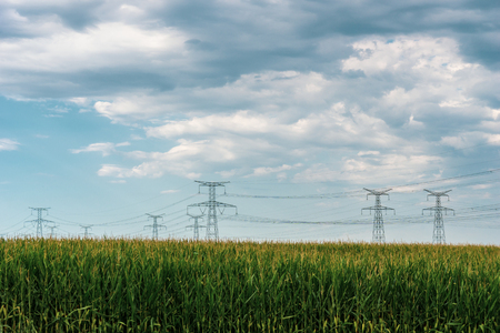 Countryside landscape. High voltage electric lines with metallic pylons over corn with on a blue cloudy sky on a day of summer, Alsace, France.の写真素材