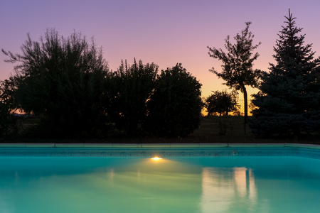 Outdoor blue liner swimming pool with lighting at dusk twilight sunset on a clear evening of summer, France.の写真素材