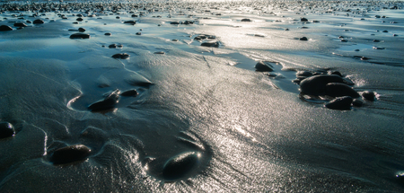 Pebbles on the beach or shore at low tide with light flares. Coastline or sea or ocean wallpaper, background or background. Nature, tranquility concept.の写真素材