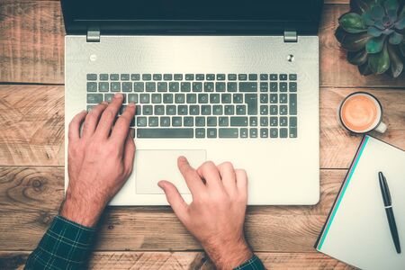 Office work top view with hands typing on a laptop. Rustic wooden desk with computer, plant, coffee and notebook. Modern workspace concepts.の写真素材