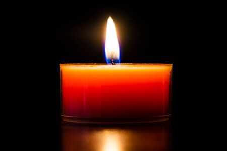 Orange burning candle in a glass tealight beautiful close-up isolated on black.の写真素材