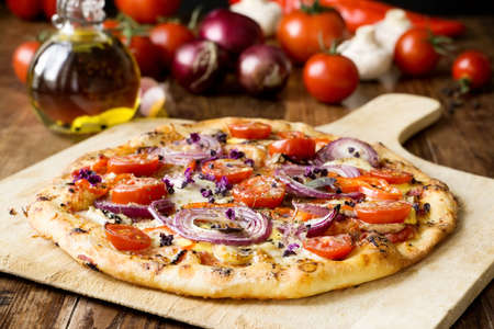 Vegetarian pizza with red onion rings, cherry tomatoes, red pepper, garlic, lilac basil flowers and hollandaise sauceの写真素材