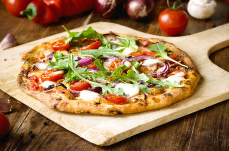 Freshly baked pizza with arugula, tomato, red onion and mozzarellaの写真素材