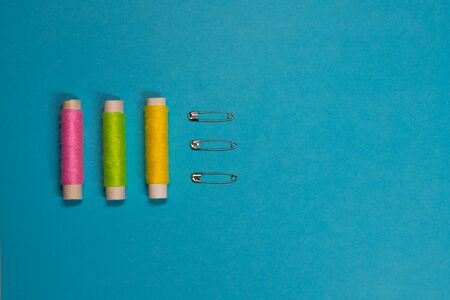 Sewing concept flat lay with cotton and safety pins on a blue background
