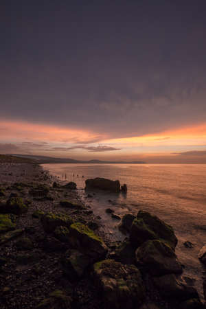 Golden hour sunset at Colwyn bay, North Wales. Warm sky and gentle waves along a rocky coastlineの写真素材